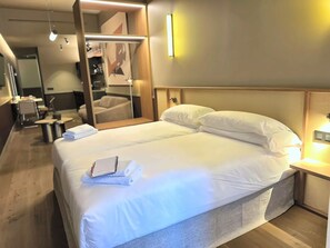 A hotel room with a neatly made bed, a bedside table with a lamp, a mirror, and a seating area with a chair and table. - La Ría Urban Apartments (Bilbao)