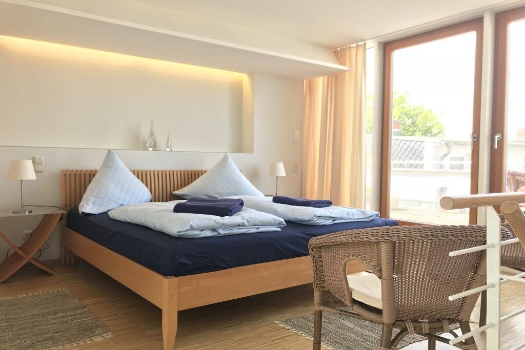 Une chambre d’hôtel avec un lit, une chaise, une table de chevet et une grande fenêtre.