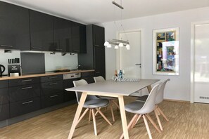A modern kitchen with dark cabinets, a wooden countertop, and a dining area with a table and chairs. - Holiday home with 2 bedrooms (Seebad Heringsdorf)