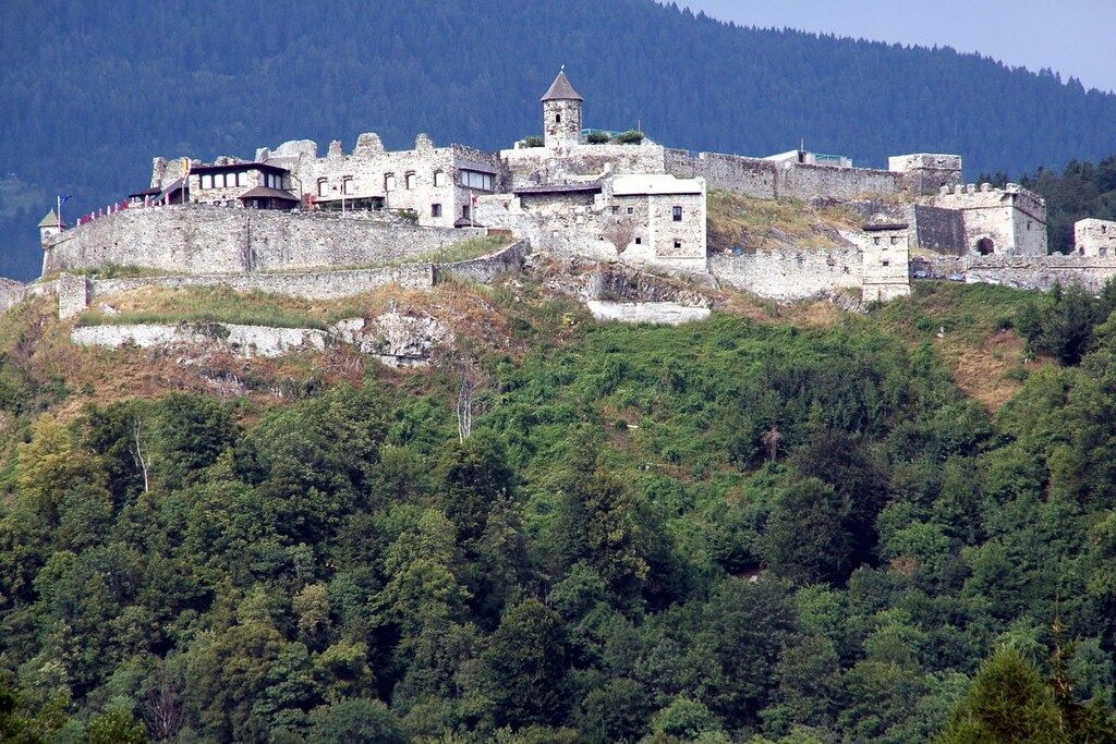 Eine historische Steinburg thront auf einem Hügel, umgeben von dichtem Wald.