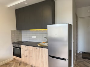 A modern kitchen with dark cabinets, a stainless steel refrigerator, a black oven, and a tiled backsplash.