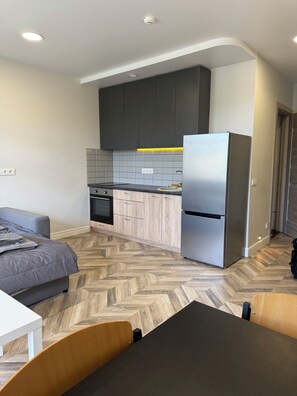 A compact kitchen with a refrigerator, a dining table, and a sofa.