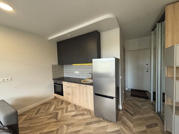 A modern kitchen with a built-in oven, a stainless steel refrigerator, and a herringbone-patterned wooden floor.