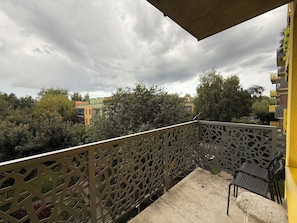 A balcony with a lattice railing, a concrete floor, and a view of surrounding buildings and trees.
