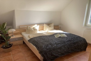 A bedroom with a bed, pillows, a bedside table, a lamp, a plant, and a window. - "Aileen" in the Riwa House (Kölpinsee)