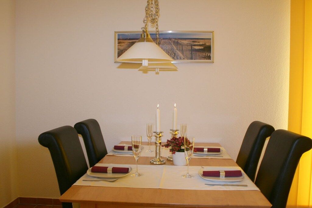 A dining table set for four with a hanging lamp, candles, and a framed picture on the wall.