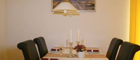 A dining table set for four with a hanging lamp, candles, and a framed picture on the wall.