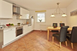 Cuina moderna amb armaris blancs, una cuina i una zona de menjador amb taula i cadires.