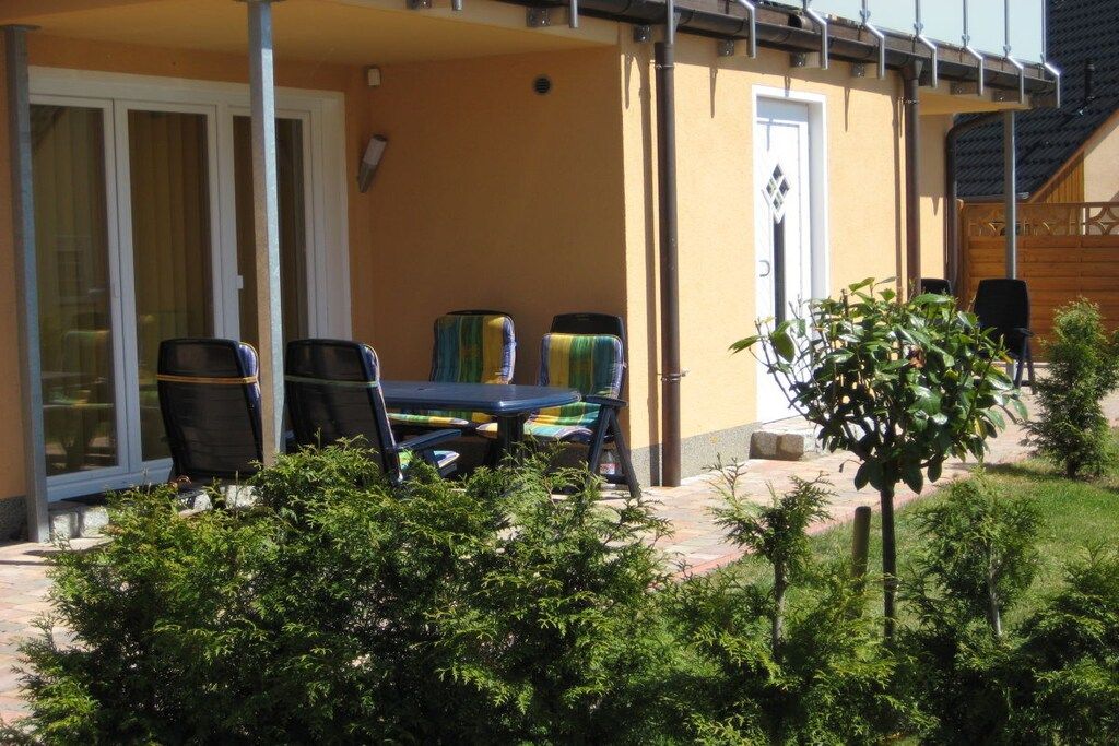 Un patio exterior con una mesa, sillas, una puerta y un árbol pequeño.