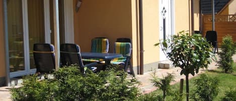 Un patio exterior con una mesa, sillas, una puerta y un árbol pequeño.