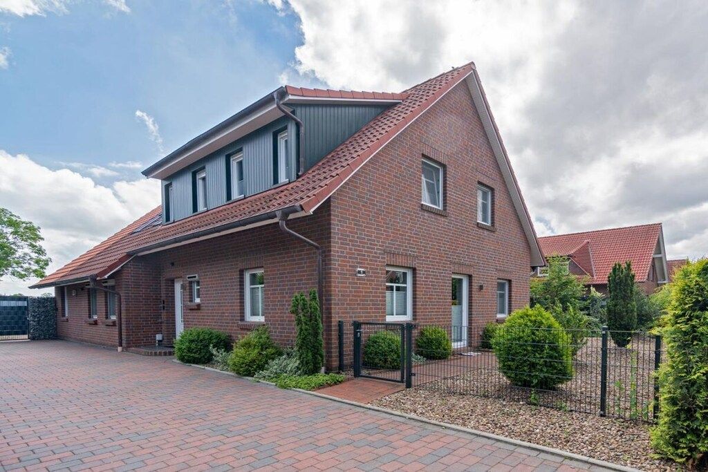 Une maison à deux étages, construite en briques, avec un toit en pente, une allée pavée et une entrée fermée par un portail.