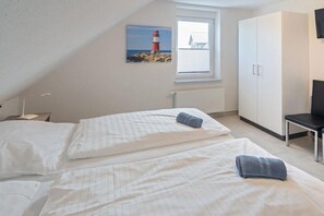 Een slaapkamer met twee bedden, een raam met uitzicht op een vuurtoren, een kledingkast en een stoel.