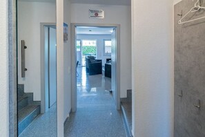 A hallway leading to a reception area with a sign above the door, a staircase to the left, and a view of the outside through the door. - Holiday home with 1 bedroom (Bensersiel)