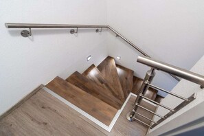 A wooden staircase with a metal handrail and a white wall. - Holiday home with 1 bedroom (Bensersiel)