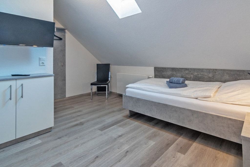 Un dormitorio con cama, una silla y una zona de kitchenette.