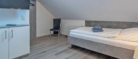 Un dormitorio con cama, una silla y una zona de kitchenette.