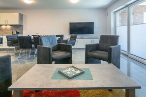 A modern living room with a flat-screen TV, comfortable seating, and a view of the outdoors. - Holiday home with 1 bedroom (Bensersiel)