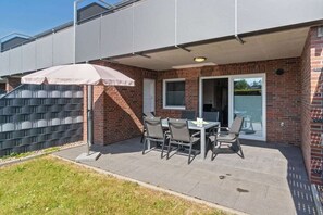 An outdoor patio area with a table and chairs, a covered seating area, and a brick building with a sliding glass door. - Holiday home with 1 bedroom (Bensersiel)