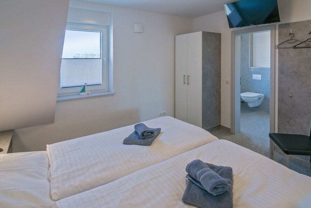 A hotel room with two beds, a television, a window, and a bathroom with a toilet.
