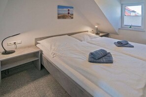 A bedroom with two beds, a desk, a lamp, and a painting on the wall. - Holiday home with 1 bedroom (Bensersiel)