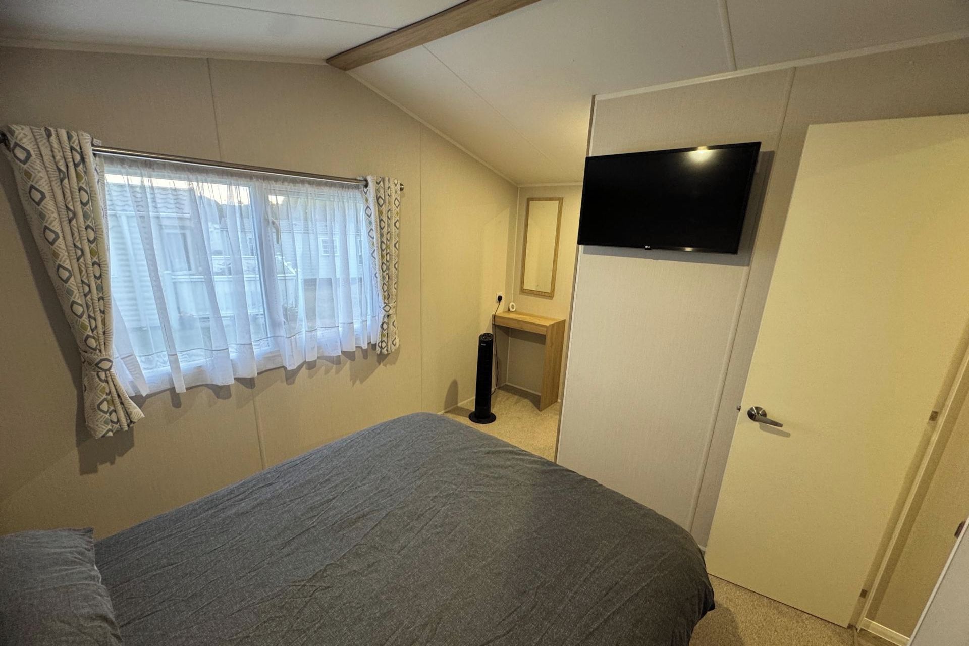 A bedroom with a bed, a TV mounted on the wall, a door, and a window with curtains.