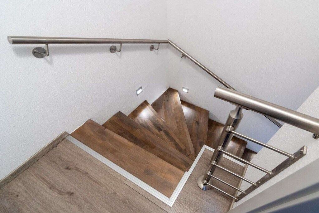 A wooden staircase with a metal handrail and a white wall.