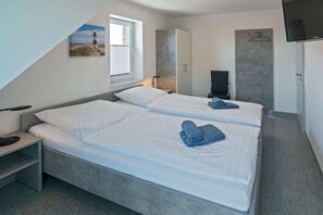 Ein Schlafzimmer mit zwei Betten, einem Fernseher und einem Gemälde eines Leuchtturms.