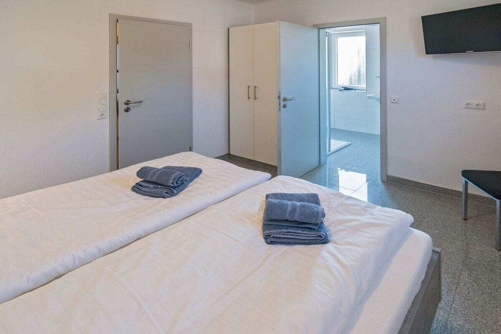 A hotel room with two beds, a wardrobe, a television, and a door leading to a bathroom.
