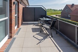 Ein Balkon mit Tisch und Stühlen, Blick auf die Landschaft und ein Backsteinhaus.