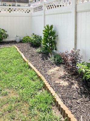 Un jardí amb una tanca de fusta, diverses plantes i una valla blanca.