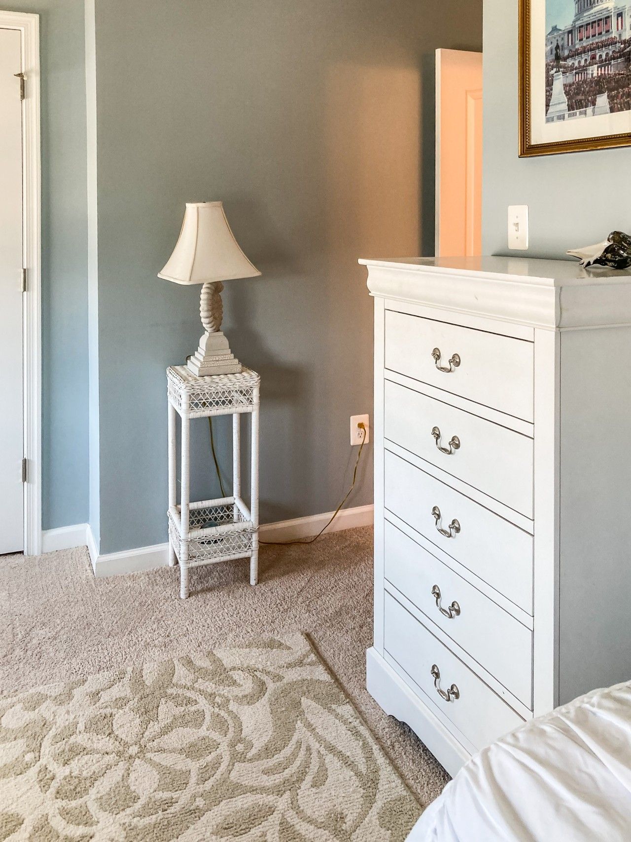 A bedroom with a white dresser, a lamp on a small table, and a patterned carpet.