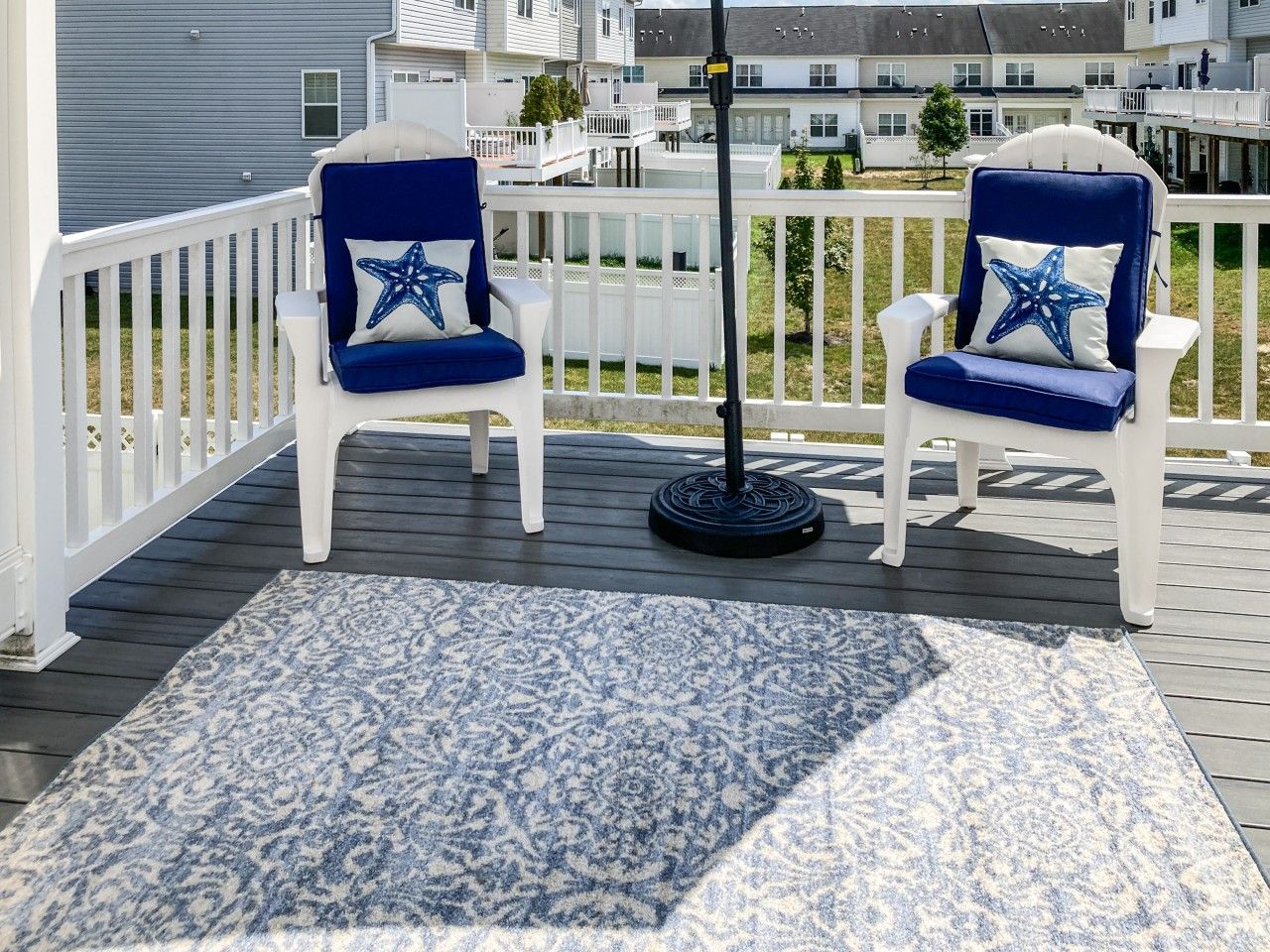 Un patio con due sedie bianche e un cuscino a forma di stella marina, un tappeto decorato e una ringhiera.