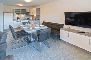 A modern kitchen with a dining area, including a table set for four, a sofa, and a TV mounted on the wall. - Holiday home with 1 bedroom (Bensersiel)