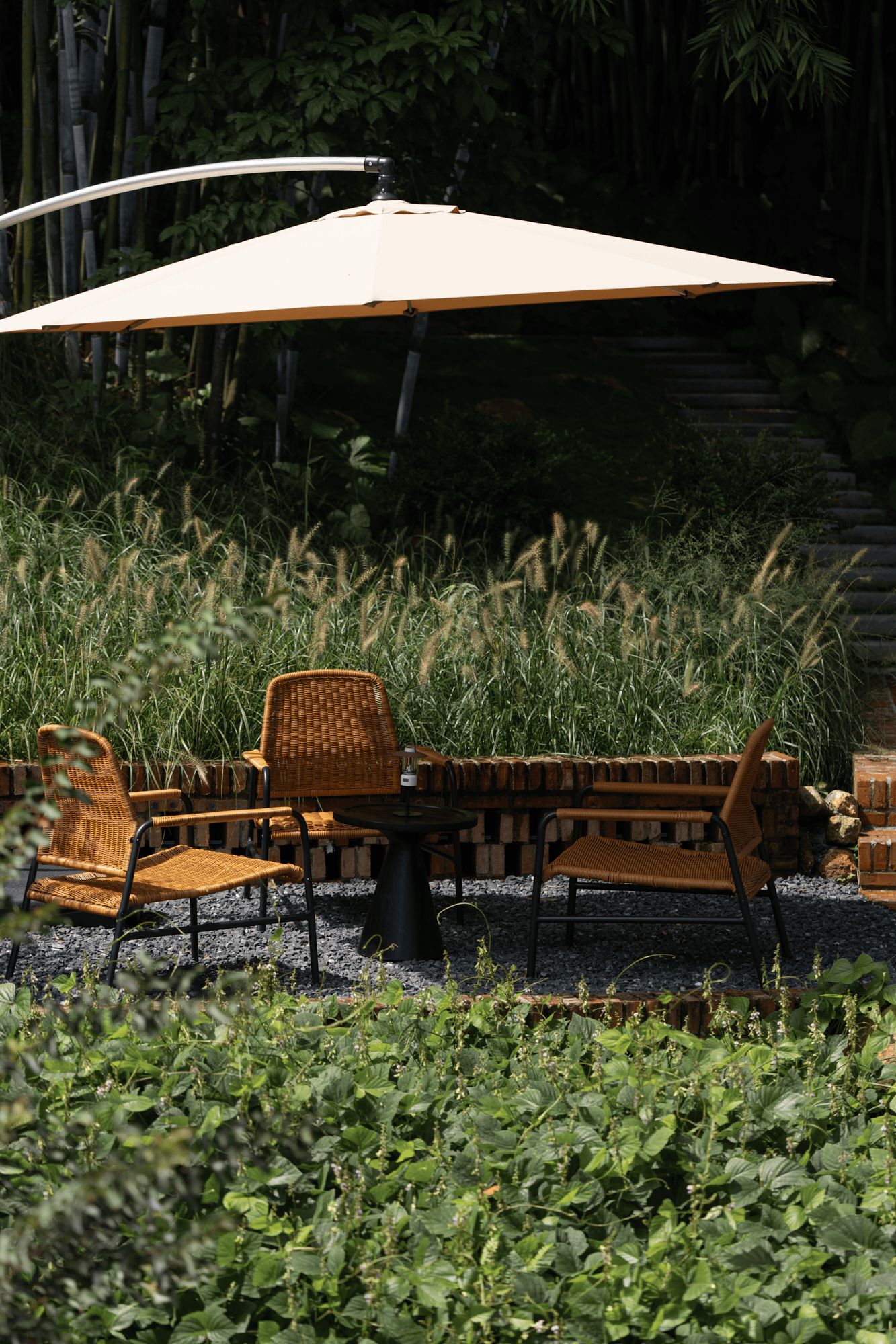 Outdoor furniture with a table and chairs, an umbrella, and a backdrop of greenery and bamboo.