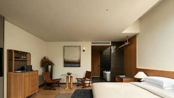 Habitación de hotel moderna con cama, escritorio, silla, una mesita y zona de ducha.