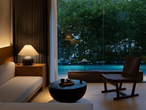 A modern living room with a sofa, a coffee table, and a chair, a lamp, and a view of a pool and trees. - SAINT LANCY HOTEL (Guangzhou)
