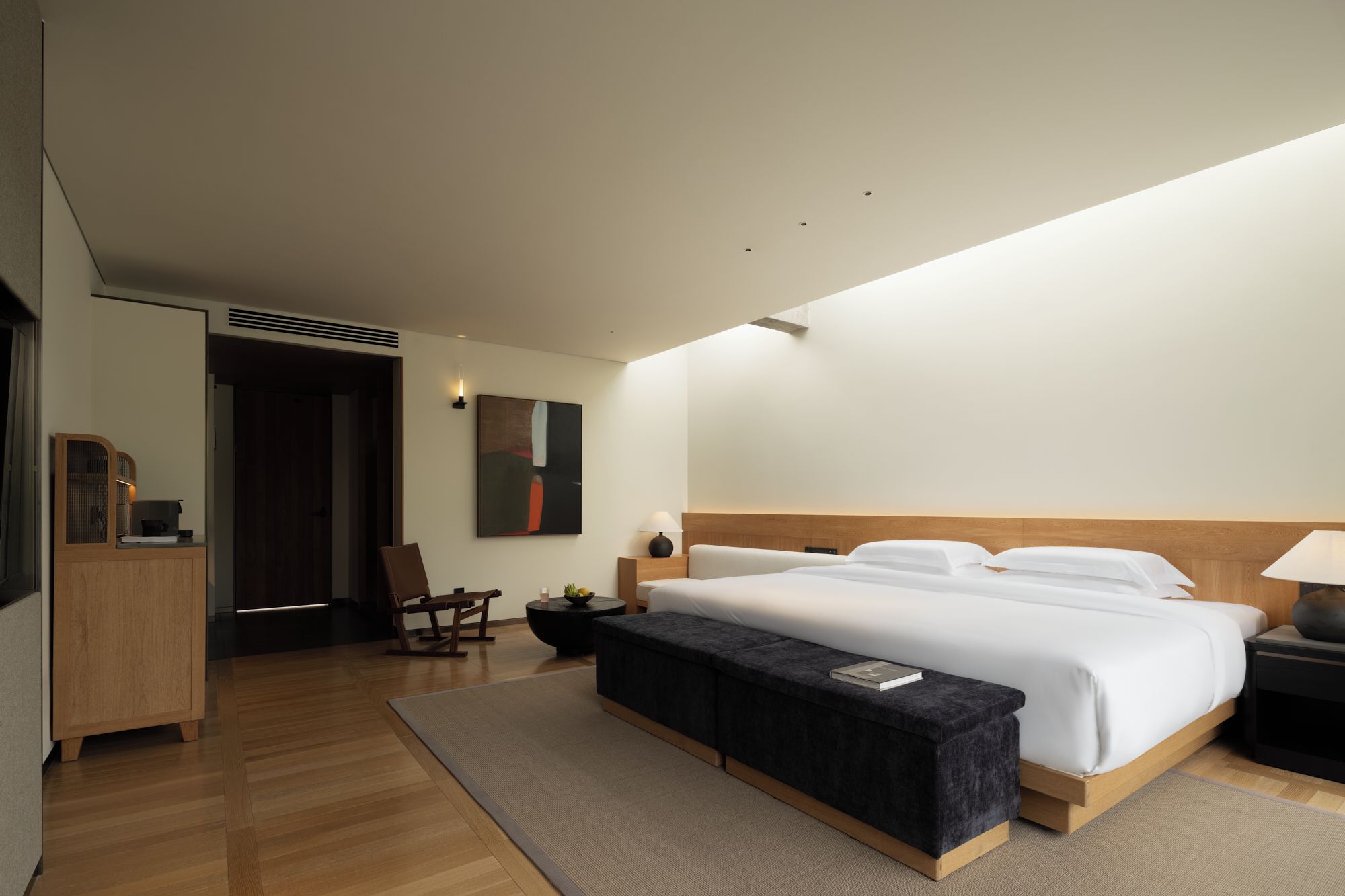 A modern hotel room with a large bed, bedside tables, a bench, a desk, and a chair.