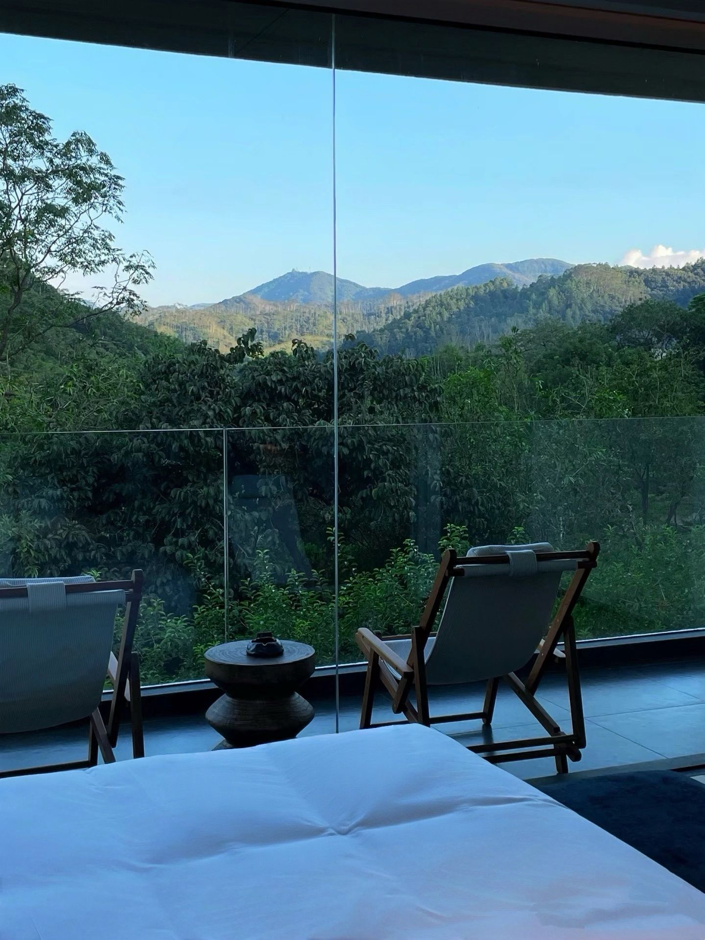 Ein Zimmer mit einem Bett, zwei Stühlen und einem kleinen Tisch, mit Blick auf eine gebirgige Landschaft.