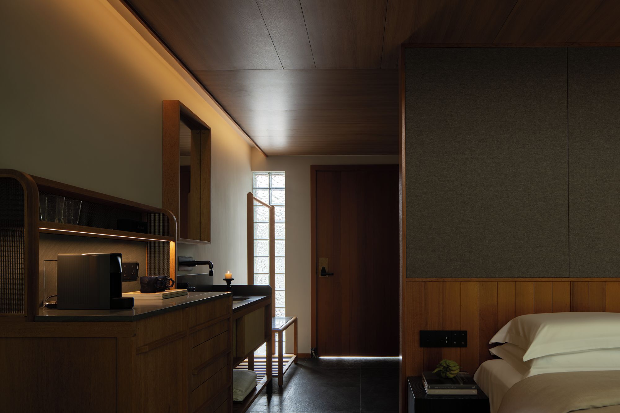 A hotel room with a wooden desk, a bed, a nightstand, and a window with a view.