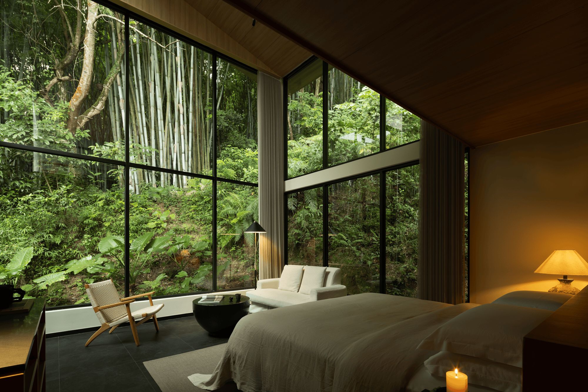 Une chambre avec une grande fenêtre, un lit, une chaise, une table et une lampe.