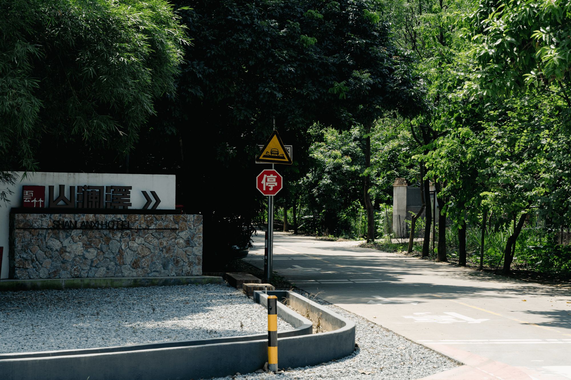 Una carretera con una señal de pare y una señal de advertencia triangular. Hay un muro de piedra con un letrero que dice 'Suan Anxi'.