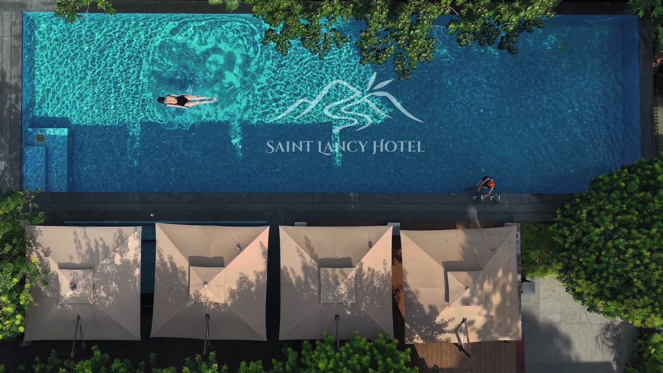 Ein Schwimmbecken mit einer schwimmenden und einer tauchenden Person, und dem Schriftzug 'SAINT LANCY HOTEL' auf der Wasseroberfläche.