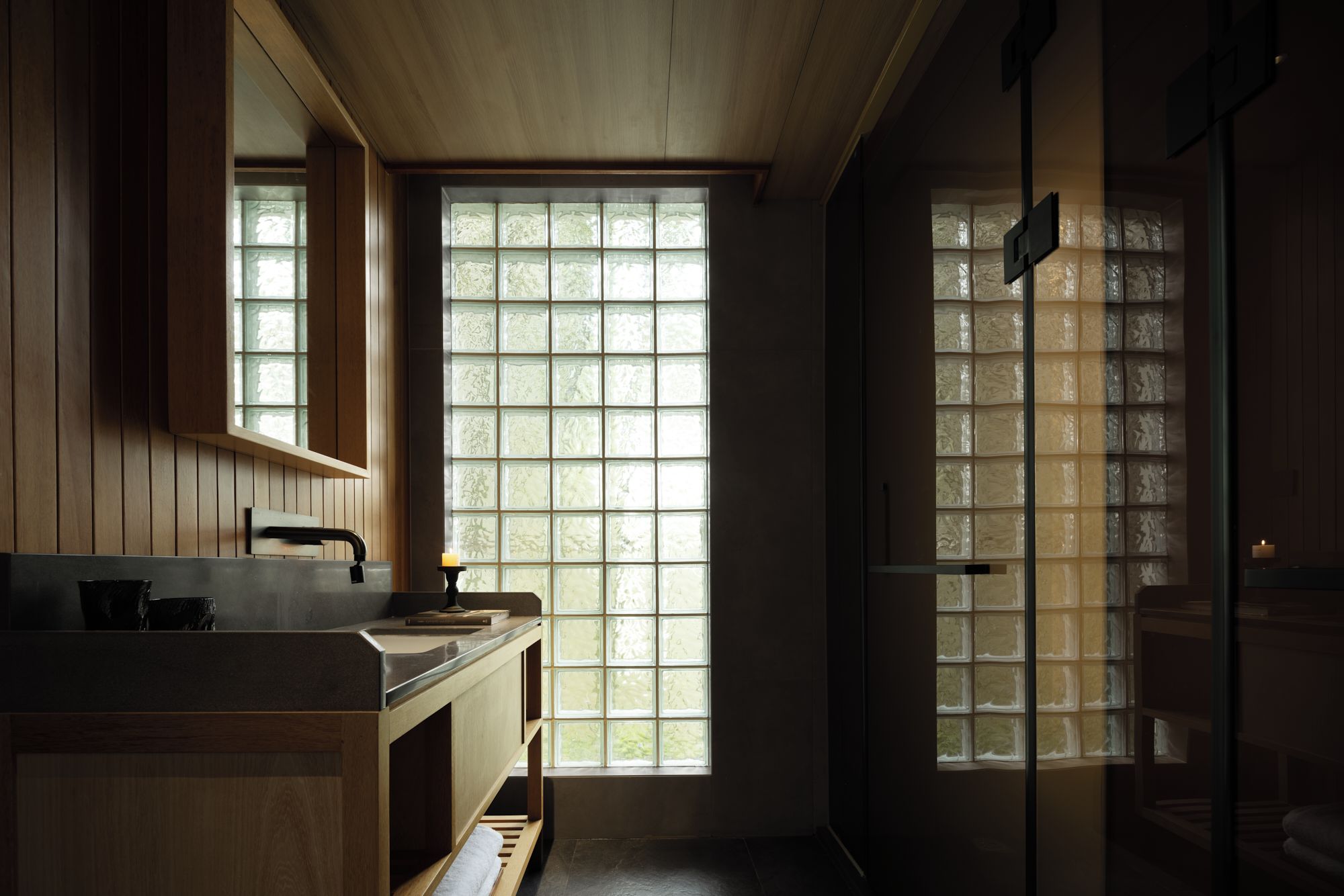 Une salle de bain avec un lambris en bois, un lavabo et une grande fenêtre dotée de panneaux en verre dépoli.