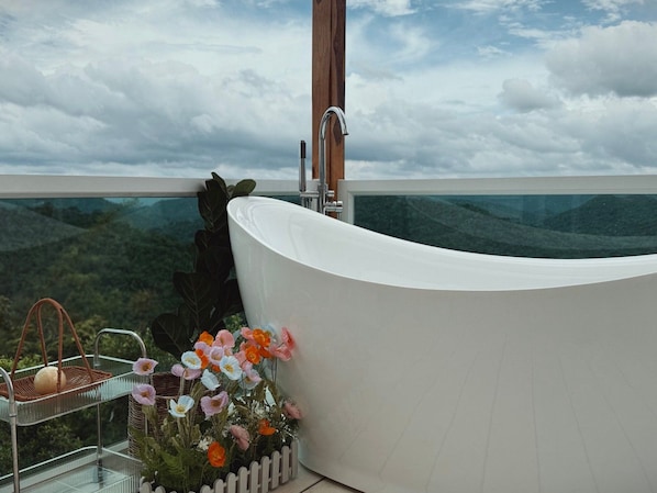 A modern bathroom with a freestanding bathtub, a glass shower enclosure, and a view of a mountainous landscape.