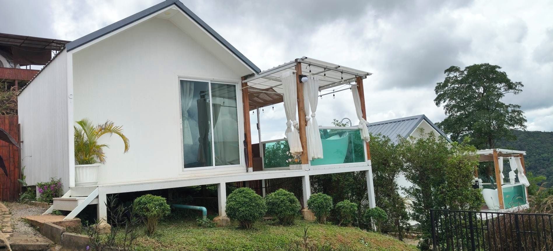 A modern two-story house with a balcony, a covered outdoor area, and a garden.