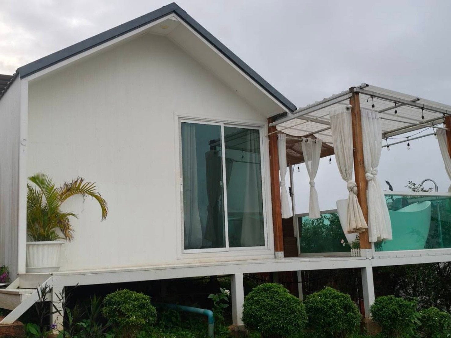 A modern house with a large glass window, a covered outdoor area with a white canopy, and a small garden with plants.