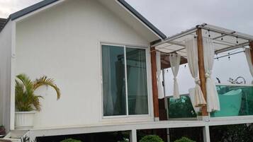 A modern house with a large glass window, a covered outdoor area with a white canopy, and a small garden with plants.