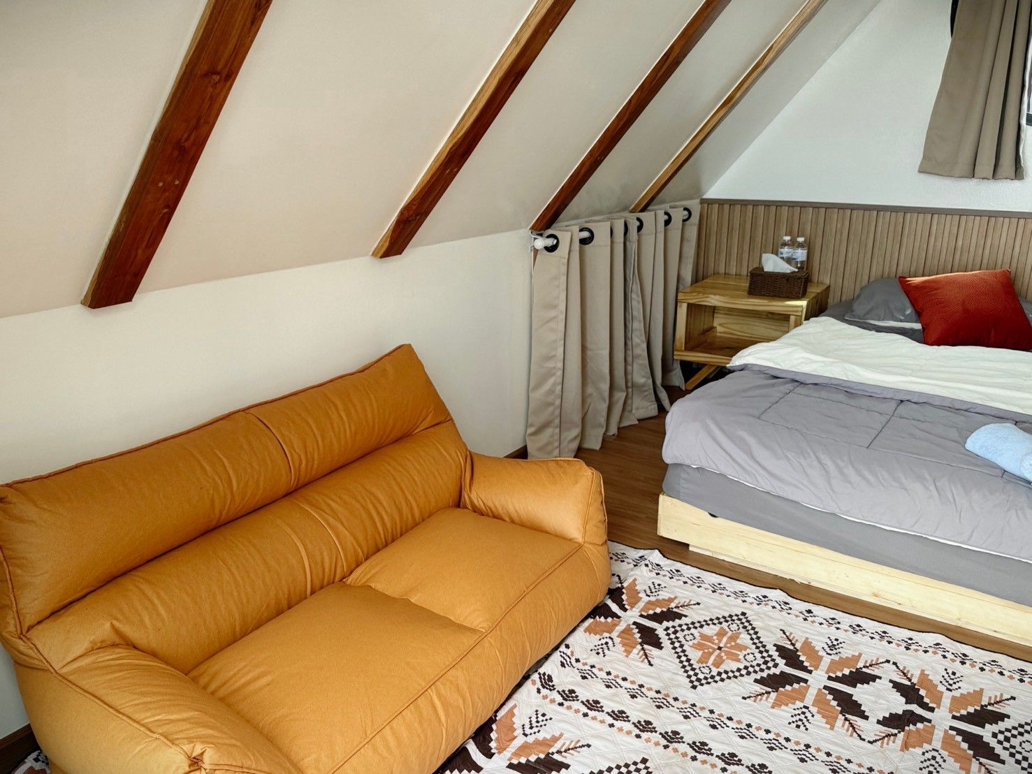 Een gezellige kamer met een slaapbank, een bed, een kamerbreed tapijt met een patroon en een houten hoofdeinde.