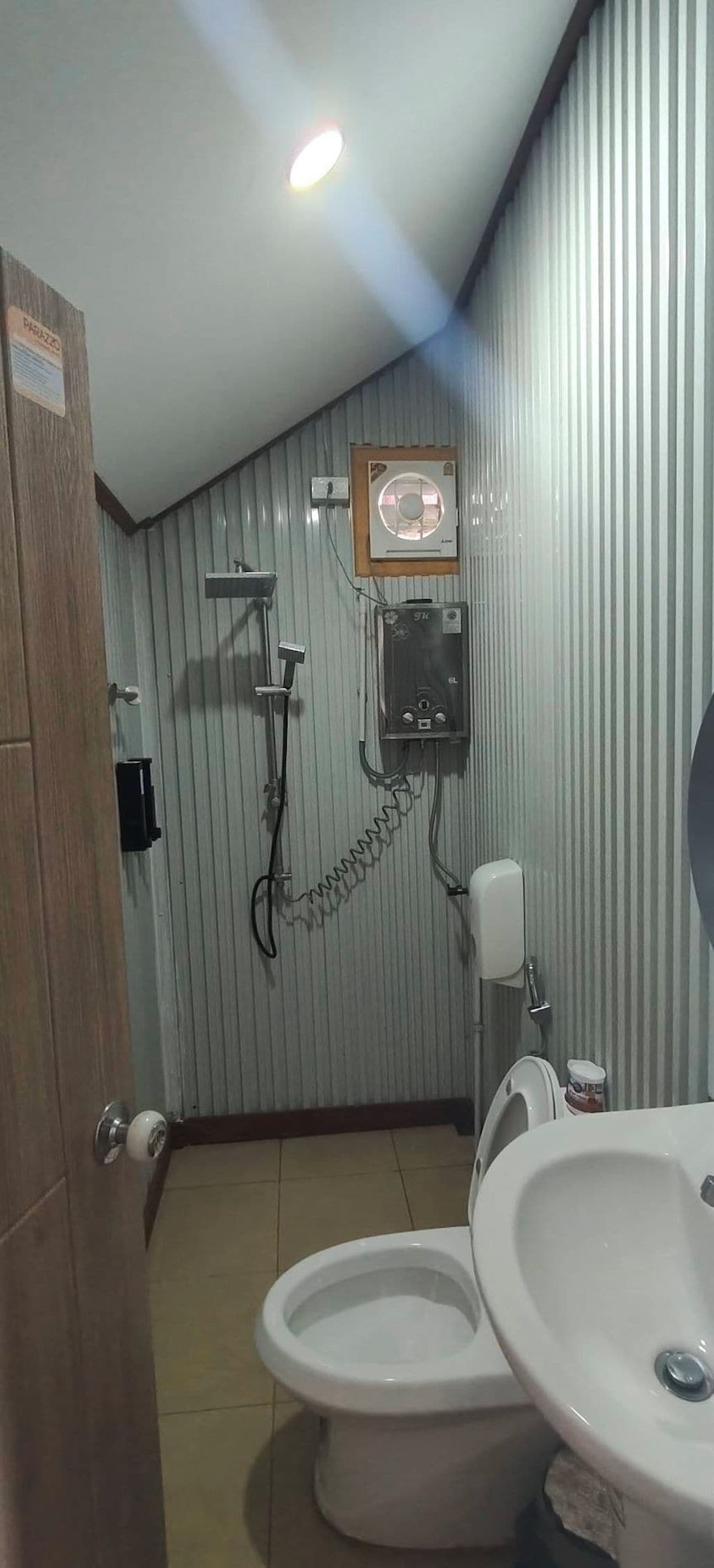 A bathroom with a toilet, a sink, a shower, and a fan on the ceiling.