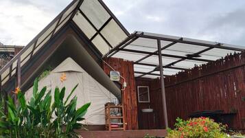 A triangular tent-like structure with a wooden bench and a small table, surrounded by greenery and potted plants.